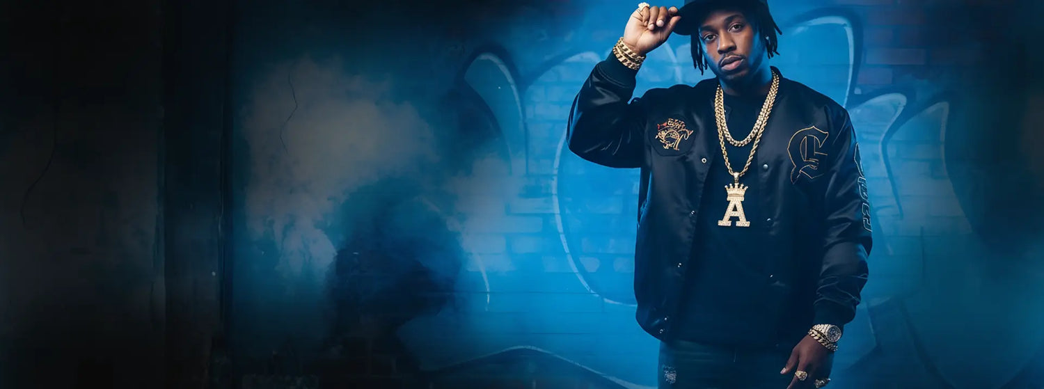 Person wearing a dark jacket with  gold chains, gold braclets, rings and hat in a blue-lit room